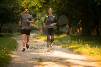Young Couple Running In Wooded Forest Area - Training And Exercising For Trail Run Marathon Endurance - Fitness Healthy Lifestyle Concept