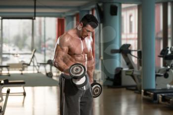 Muscular Young Man Doing Heavy Weight Exercise For Biceps With Dumbbells In Modern Fitness Center