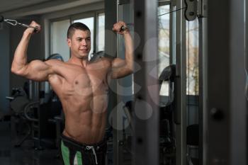 Young Bodybuilder Is Working On His Biceps With Cable Crossover In A Dark Gym