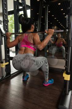Young Latin Woman Working Out Legs With Barbell In Fitness Center - Squat