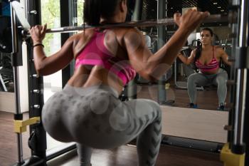 Young Latin Woman Working Out Legs With Barbell In Fitness Center - Squat