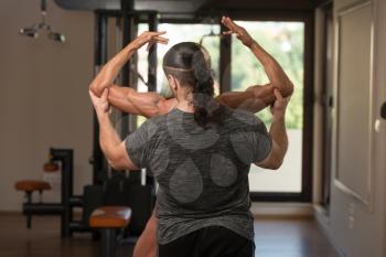 Portrait Of A Middle Aged Woman Posing Bodybuilding Poses In Modern Fitness Center And Partner Correct Her
