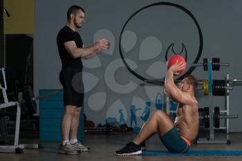 Young Man With Personal Trainer Doing Medicine Ball Exercises