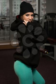 Young Sexy Woman In Black Hooded Sweatshirt Posing In Gym