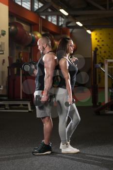Strong Young Couple Working Out With Dumbbells For Biceps In The Gym With Exercise Equipment