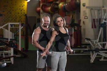 Personal Trainer Showing Young Woman How To Train Shoulders With Dumbbels In The Gym