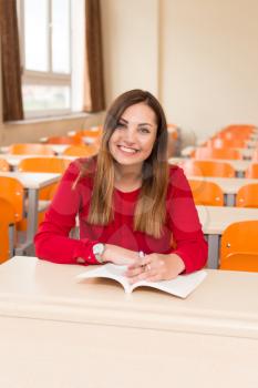 Portrait Of Young Female College Student With Book Sitting In Classroom Alone