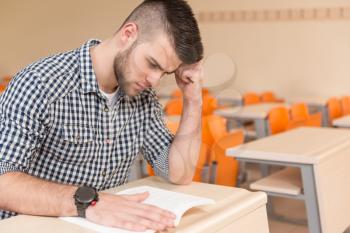 Portrait Of Young Male College Student With Book Sitting In Classroom Alone