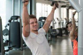 Young Couple Doing Exercise For Back On Machine In The Gym