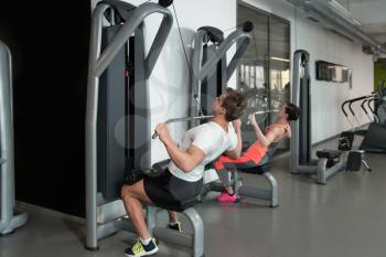 Strong Young Couple Doing Exercise For Back On Machine In The Gym