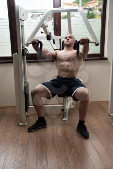 Young Man In Gym Exercising On Machine Chest Press