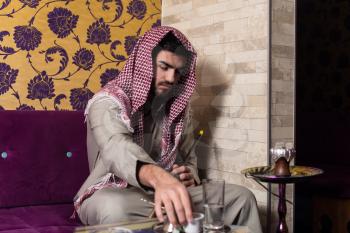 Islamic Man Smoking The Traditional Hubble-Bubble Or Hookah While Drinking Coffee