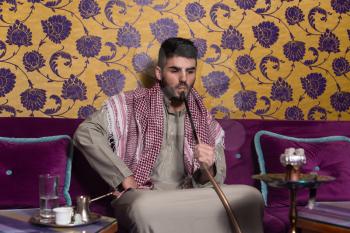 Islamic Man Smoking The Traditional Hubble-Bubble Or Hookah While Drinking Coffee