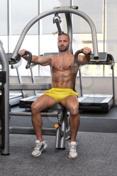 Young Man In Gym Exercising On Machine Chest Press