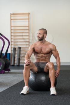 Portrait Of A Muscular Man Resting On Pilates Ball In Fitness Gym