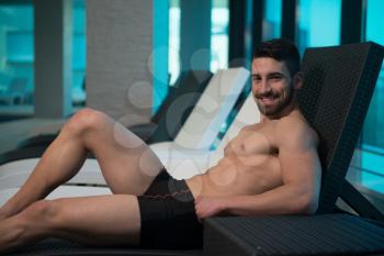 Young Man Resting On Sun Loungers By Swimming Pool And Flexing Muscles