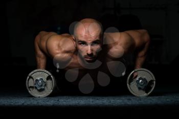 Young Adult Athlete Doing Push Ups With Dumbbells As Part Of Bodybuilding Training In A Dark Room