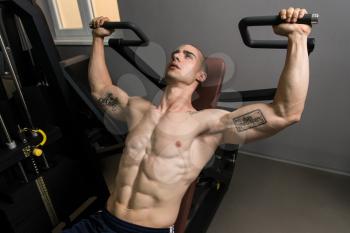 Young Bodybuilder Doing Heavy Weight Exercise For Shoulders On Machine