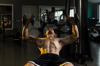 Muscular Man Doing Exercise For Chest With Dumbbells In A Gym
