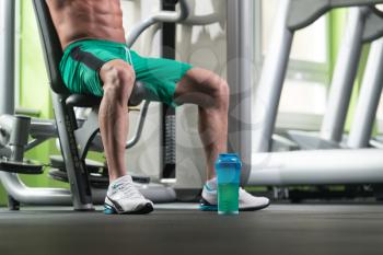 Close Up Of A Muscular Man Legs Resting After Exercise And Shaker At The Floor