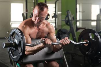 Muscular Man Doing Heavy Weight Exercise For Biceps With Barbell In Gym