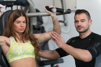 Personal Trainer Showing Young Woman How To Train Shoulders On Machine In The Gym