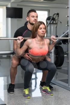Personal Trainer Showing Young Woman How To Train Barbell Squats Exercise In A Gym