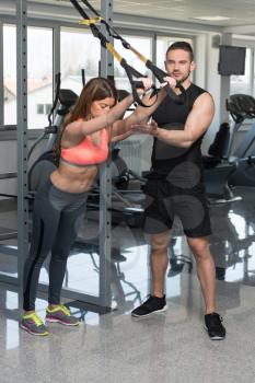 Personal Trainer Showing Young Woman How To Train With Trx Fitness Straps In A Health And Fitness Concept