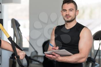 Personal Trainer Working With A Young Man At The Gym Writing Notes On A Clipboard In A Health And Fitness Concept