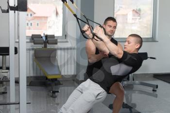 Personal Trainer Showing Young Man How To Train With Trx Fitness Straps In A Health And Fitness Concept