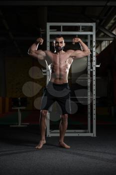 Young Man Standing Strong In The Gym And Flexing Front Double Biceps Pose - Muscular Athletic Bodybuilder Fitness Model Posing Exercises