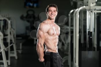 Young Man Standing Strong In The Gym And Flexing Side Triceps Pose - Muscular Athletic Bodybuilder Fitness Model Posing Exercises