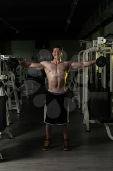 Young Man Exercising Shoulders With Dumbbells And Flexing Muscles - Muscular Athletic Bodybuilder Fitness Model Exercises