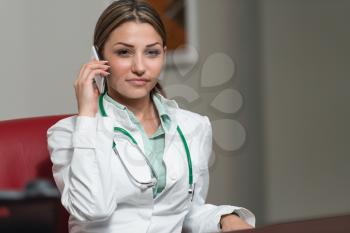 Indoor Portrait Of A Beautiful Happy Brunette Female Doctor Talking On Her Cell Phone - Healthcare Worker Working Online