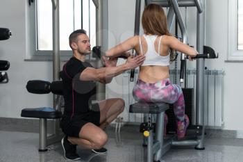 Personal Trainer Showing Young Woman How To Train Back On Machine In The Gym