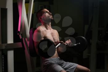 Young Muscular Man Doing Heavy Weight Exercise For Biceps With Barbell In Gym