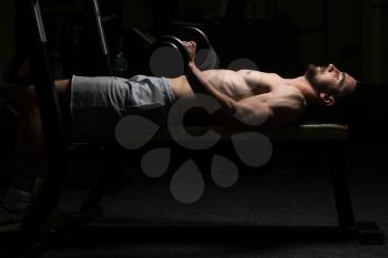 Young Muscular Man Doing Heavy Weight Exercise For Lower Arm With Dumbbells In Gym