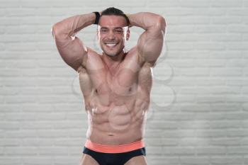 Young Man Standing Strong On White Bricks Background With Copyspace And Flexing Muscles - Muscular Athletic Bodybuilder Fitness Model Posing After Exercises