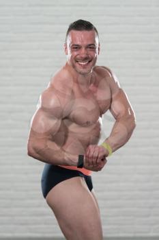 Young Man Standing Strong On White Bricks Background With Copyspace And Flexing Muscles - Muscular Athletic Bodybuilder Fitness Model Posing After Exercises