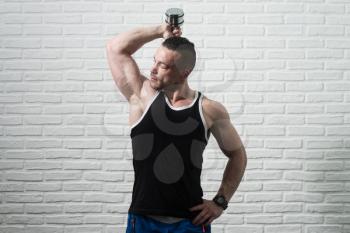 Young Man Working Out Triceps With Dumbbells On White Bricks Background With Copyspace