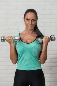 Attractive Woman Working Out Biceps With Dumbbells On White Bricks Background With Copyspace - Dumbbell Concentration Curls