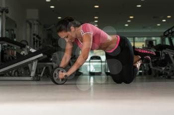 Attractive Woman Exercising With Wheel Roller For Abs On Floor In Gym As Part Of Fitness Training