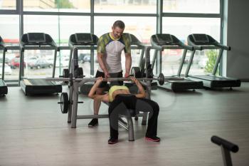 Personal Trainer Showing Young Woman How To Train Chest On Bench In The Gym
