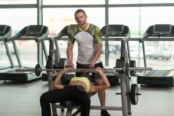 Personal Trainer Showing Young Woman How To Train Chest On Bench In The Gym