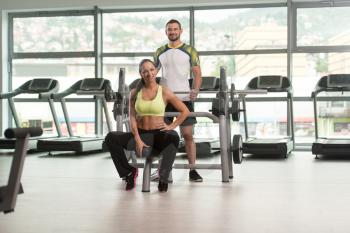 Portrait Of Fit Couple Together Training Chest On Becnh With Weights In A Gym And Looking Positive