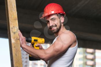 Successful Male Architect At A Building Site Trying To Drill A Large Wood Plank