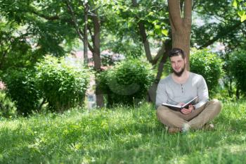 Adult Muslim Man Is Reading The Koran Outside In A Park