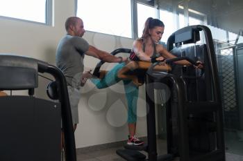 Personal Trainer Showing Young Woman How To Train Legs On Machine In The Gym