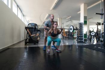 Personal Trainer Showing Young Woman How To Train Barbell Squats In The Gym