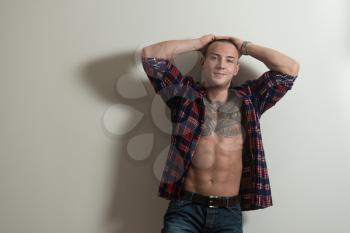 Portrait of a Tattoo Man In Shirt Showing His Abs Standing Isolated on Gray Background